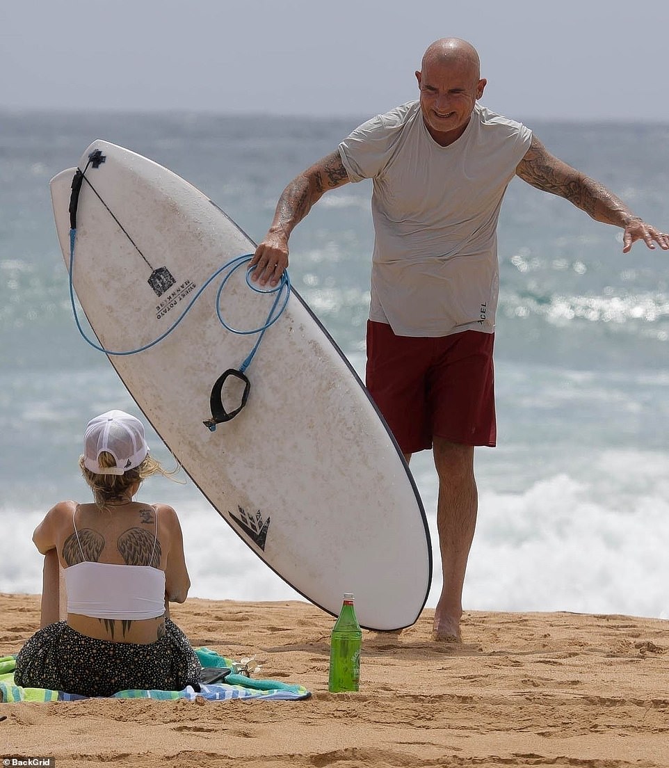 Hope you're not on board: Dominic walked over to his wife who was sitting on a blue, green and white towel as she showed off her wing tattoos on her back