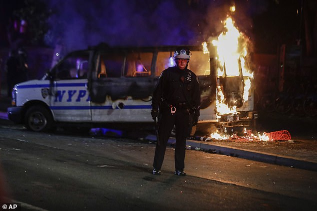 A police officer watches a crowd as a police vehicle burns near New York's Fort Greene Park after protesters gathered outside Barclays Center over the death of George Floyd, May 29, 2020