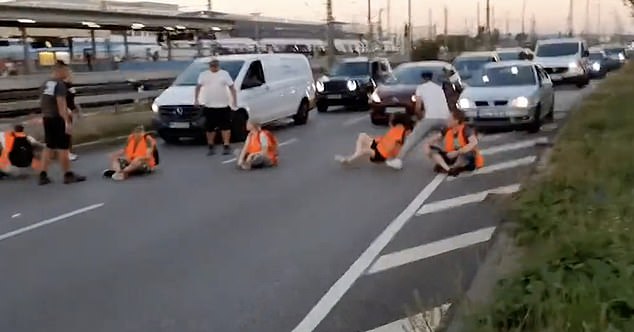 The man is seen pulling the protester off the road as other irritated motorists look on