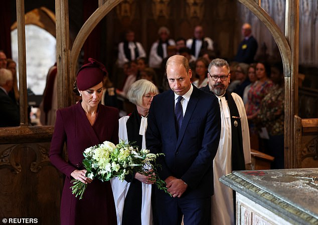 Prince William and Kate walk forward to place flowers next to a framed photo of the late Queen Elizabeth II during a service at St David's Cathedral in Pembrokeshire this afternoon