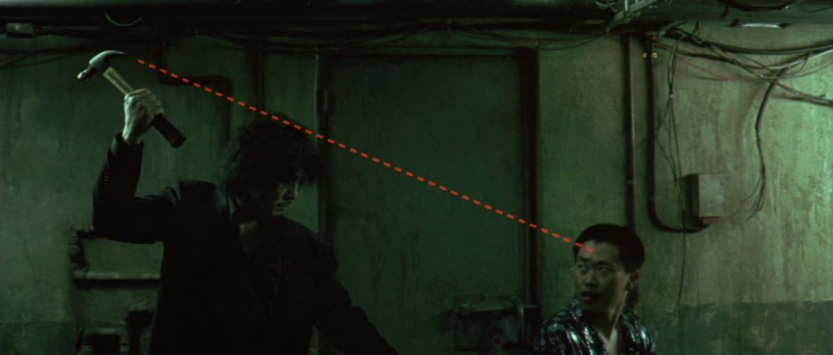 Choi Min-sik aims a hammer at the head of a man sitting in a dark hallway, with a cartoonish dotted line extending from the head of the hammer to the man's forehead in Oldboy.