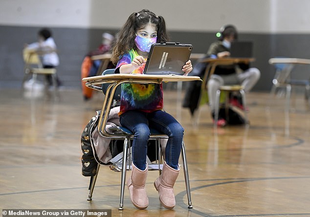 In January 2021, a child wearing a face mask is seen going to school, with socially distanced desks