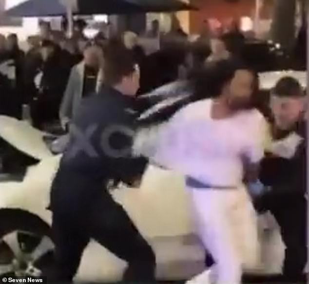 Creepy footage shows Khan, dressed all in white, sitting on the roof of the Toyota for several minutes before police officers take him down and arrest him (pictured)