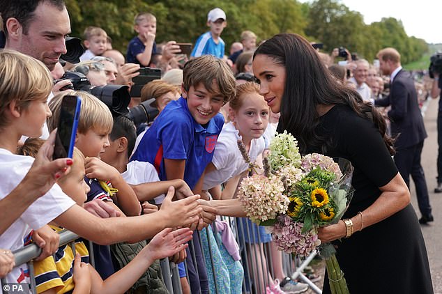 Meghan gestured to a royal aide that she was happy to continue gathering the flowers in her arms, before being approached by a second staff member, who appeared to tell her to take them away.