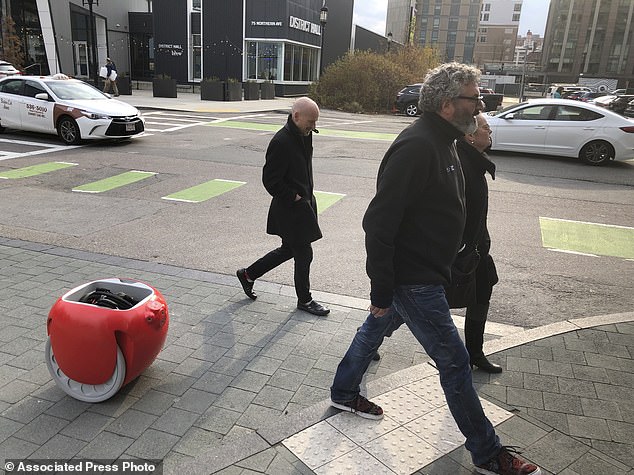 Piaggio Fast Forward CEO Greg Lynn (center) is followed by his company's Gita carrying robot as he crosses a street in Boston.  The two-wheeled machine wears a backpack and uses cameras and sensors to track its owner