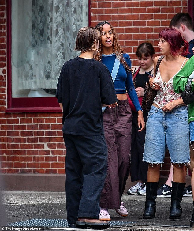 The trio waited on a street corner until the light turned green.  Malia wore a midriff-baring blue top, nylon cargo pants and a light blue bag over her right shoulder