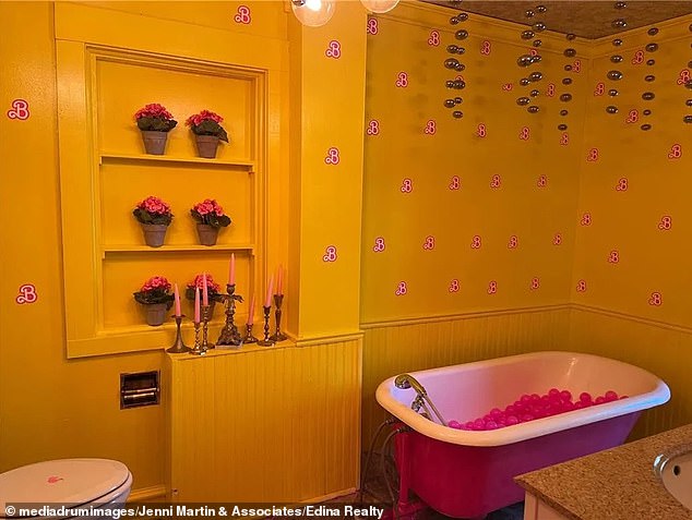 The bathroom pictured is painted yellow and the wallpaper features the iconic B logo, which stands for Barbie