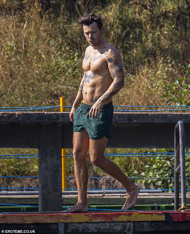 Impressive: The 29-year-old singer went shirtless, showing off his impressive abs and his array of tattoos on his arms and chest as he walked barefoot along the embankment