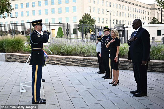 Jill Biden stands with her hand over her heart as a lone trumpeter played Taps.  General Mark Milley and Secretary of Defense Lloyd Austin saluted