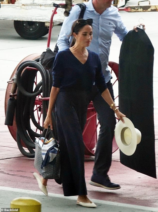 The Duchess of Sussex held on to her signature hat and carried her handbag containing a file and a silk scarf.  Her security had a suit bag and backpack