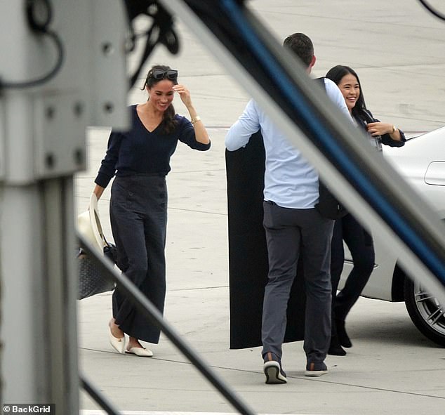 Meghan appears to be laughing with two assistants as they carried her belongings to LAX last night