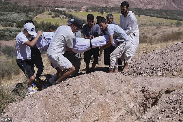 A group of men carry the body of a local resident who died in the earthquake, to be placed in a freshly dug grave