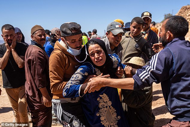 Relatives hold a woman as she is overcome with grief as her husband's body is pulled from beneath a collapsed house