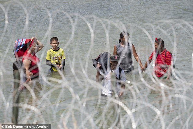 Migrants – including young children – from Central America search for an opening in the concertina wire barrier south of Eagle Pass, where a series of 1,000-foot-long buoys have been placed in the river to prevent them from crossing the Rio Grande River into Texas