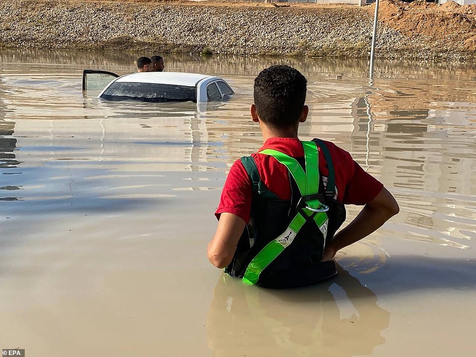 A rescue worker stands in high water next to a completely submerged car.  It has been three days since the devastating floods that hit eastern Libya with the most force