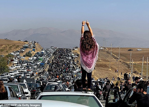 An unveiled woman stands on top of a car as thousands of people protest in Iran, October 26