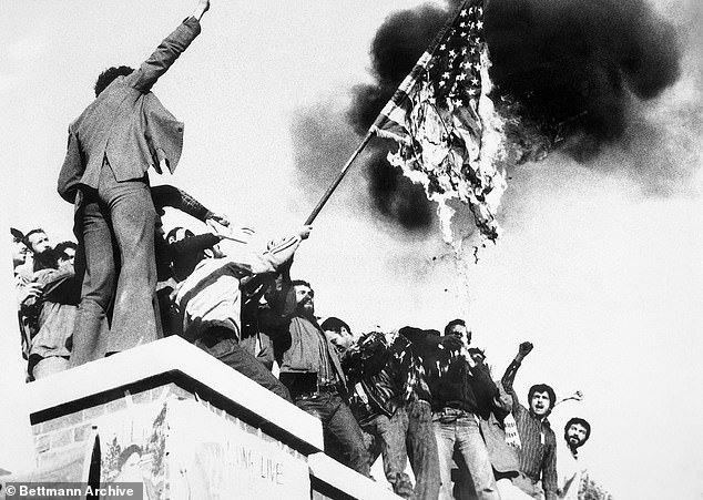 Ed Johnson, an accomplished linguist who is fluent in five languages, was identified as the second officer who helped the diplomats walk free amid the Iran hostage crisis.  Pictured: Students burn an American flag after storming the US embassy in Tehran in 1979