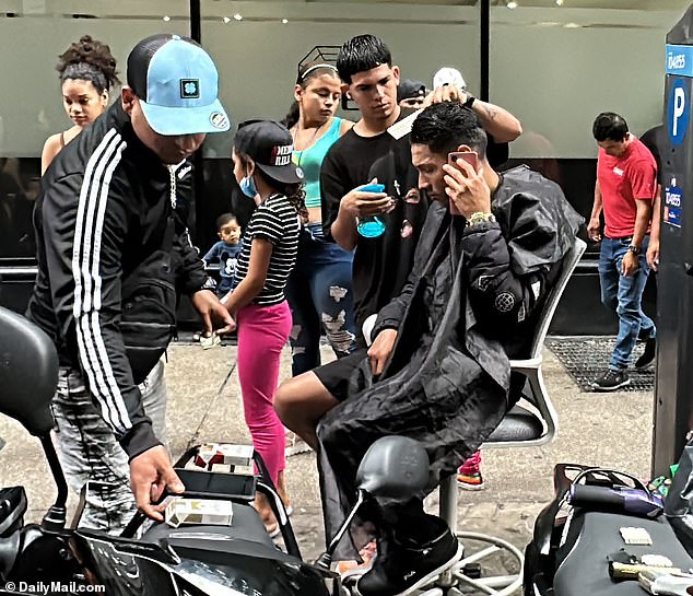 A hairdresser cuts the hair of migrants outside the Roosevelt Hotel in New York, where they are being housed, on August 23