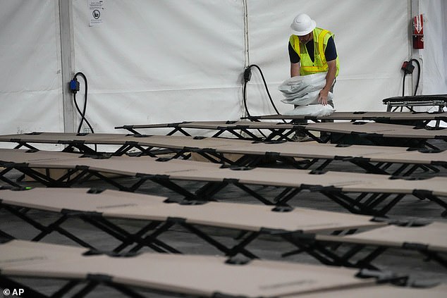 A contractor places bags containing a pillow, towel and sheets on cots in the dormitory tent and shelter in the parking lot of Creedmoor Psychiatric Hospital in Queens