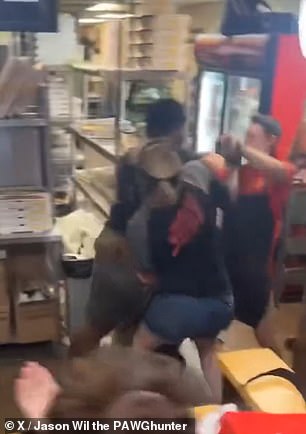 The black man walks forward and knocks the employee to the ground while two other employees, including a woman, grab the man