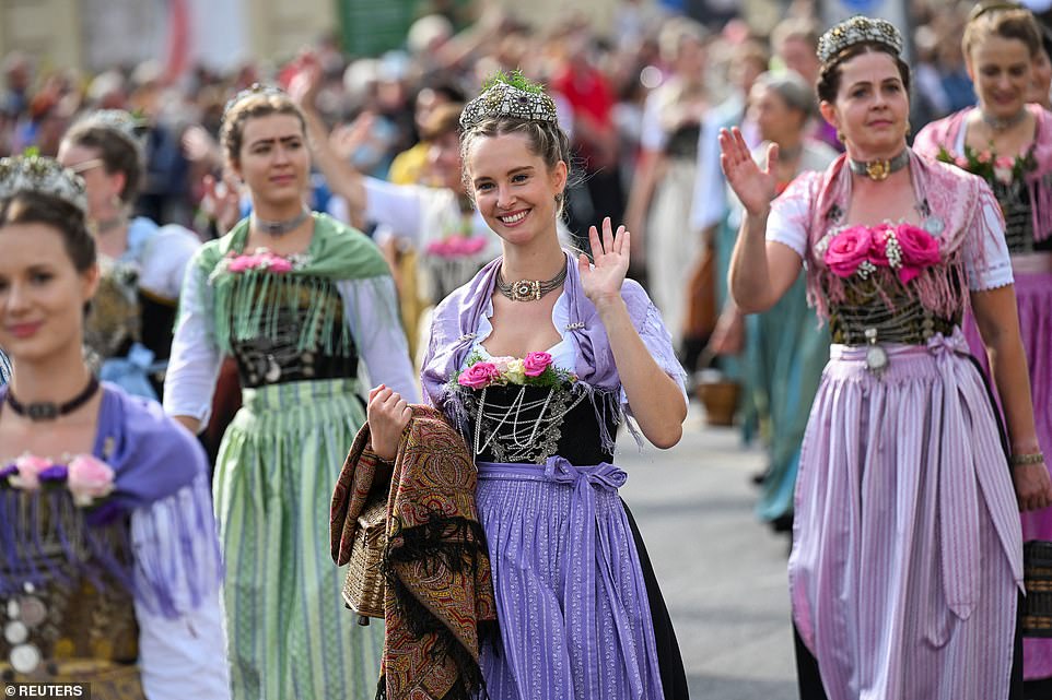 Women dressed in 'dirndls', a traditional dress consisting of a low-cut bodice, a blouse and a high-waisted skirt, wave to the crowd during the parade