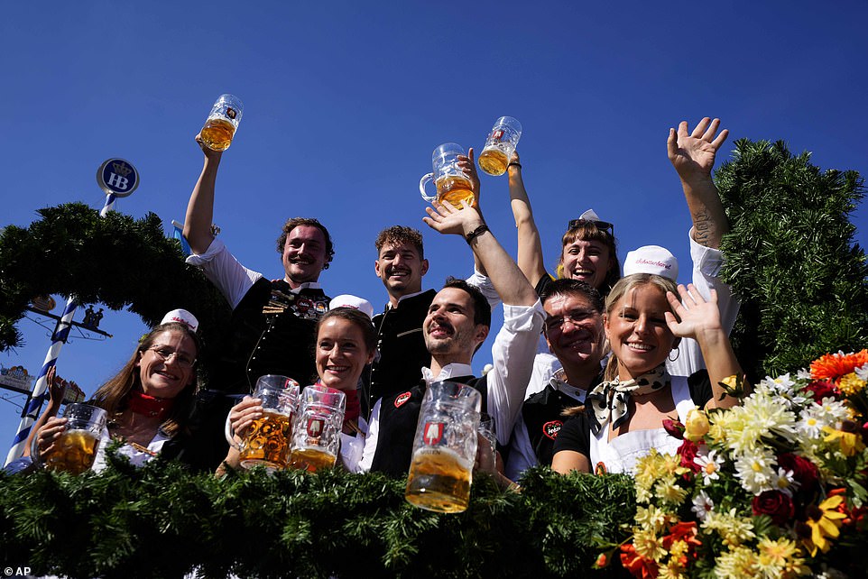 Waitresses and waiters from the 'Schottenhamel' beer tent show off their beer mugs in the sun