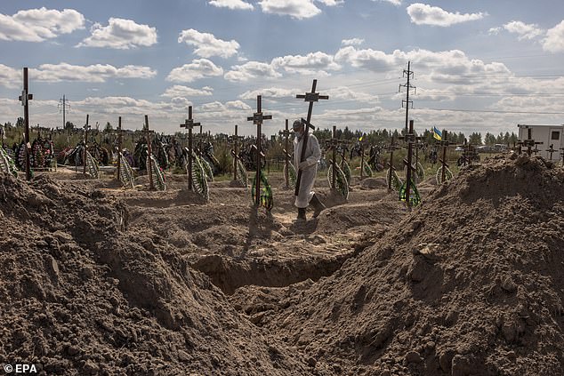 A worker carries a cross during a funeral ceremony for unidentified persons who died in the Bucha district at the time of the Russian occupation, at a cemetery in Bucha, northwest of Kiev