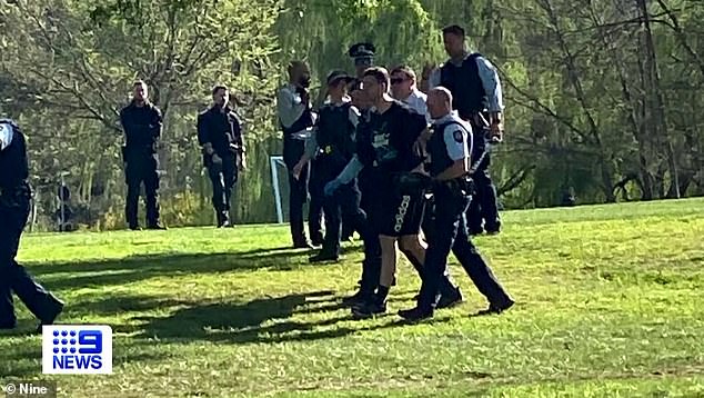 AFP officers lead Ophel away after he was arrested at the ANU's Fellow Oval on Monday afternoon