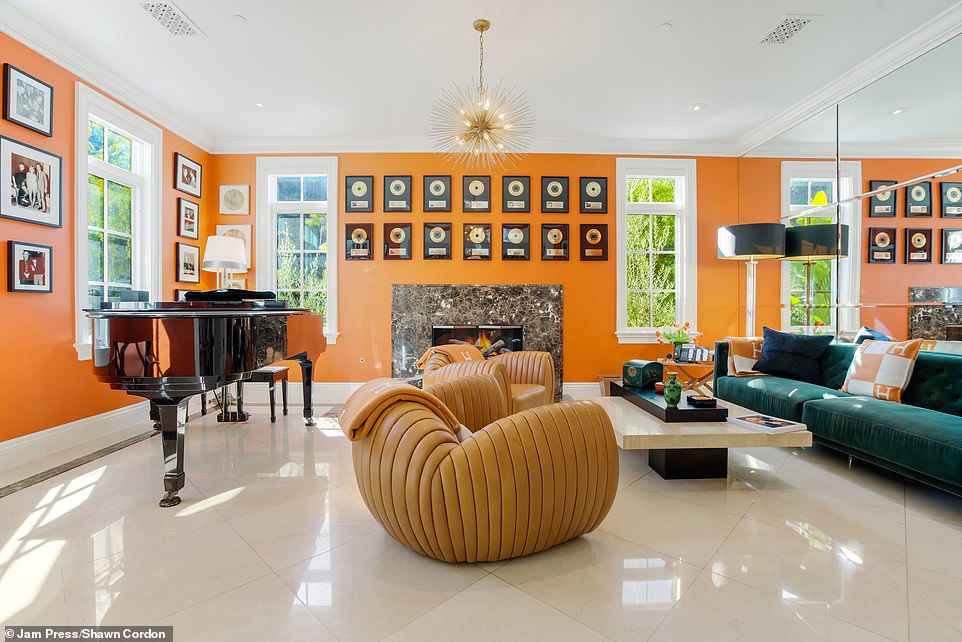 One of the living rooms stands out with its bright orange walls, green suede sofa, mirrored wall, light brown leather reading chairs and grand piano.