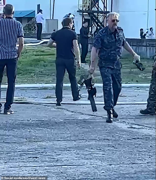 Several armed Russian men dressed in military fatigues are seen carrying away debris from a drone that attacked the Sochi fuel depot early on September 20, 2023.