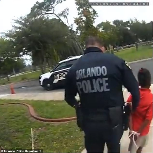 An officer is seen leading Kaia out of school in wrist restraints.