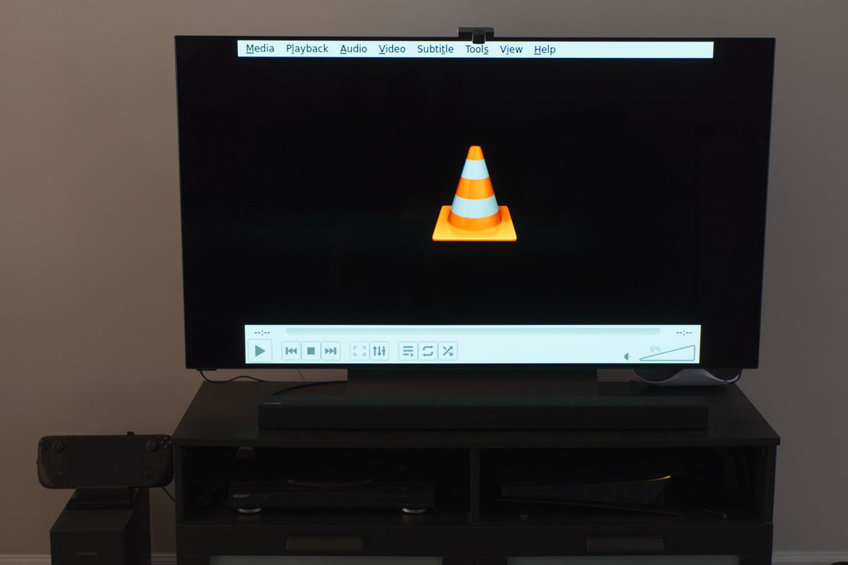 A photo of a 55-inch TV with the VLC media player application displayed on it.  It's powered by a Steam Deck with a USB DVD drive plugged into its dock.