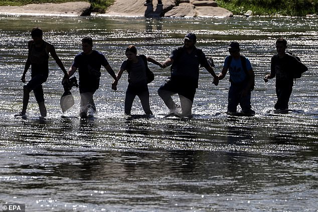 Migrants are seen holding hands Thursday to wade across the Rio Grande and arrive at Eagle Pass