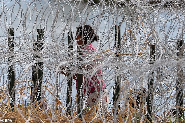 A woman climbs onto the riverbank, with barbed wire blocking access