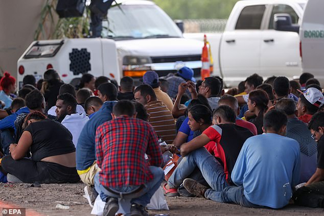 Migrants sit under a bridge in Eagle Pass Thursday awaiting processing