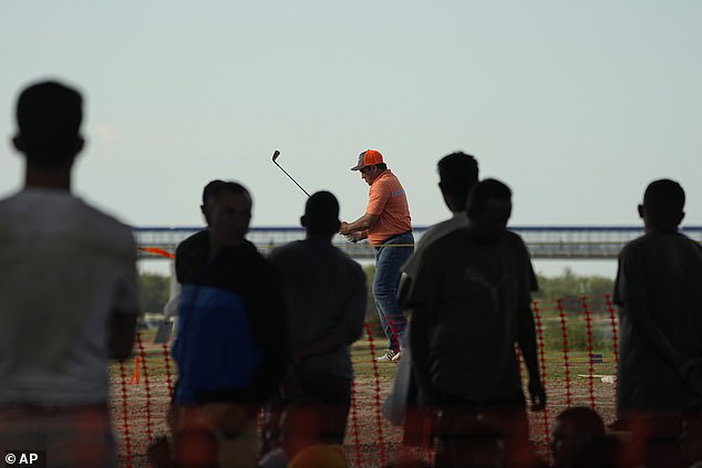 An Eagle Pass resident plays golf Thursday as migrants look on