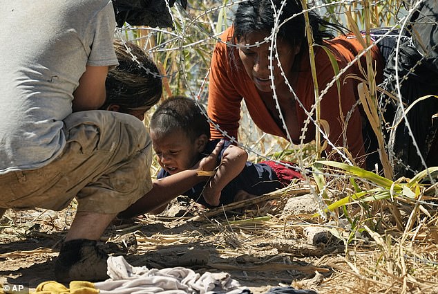 A baby is passed under the barbed wire near Eagle Pass on Thursday