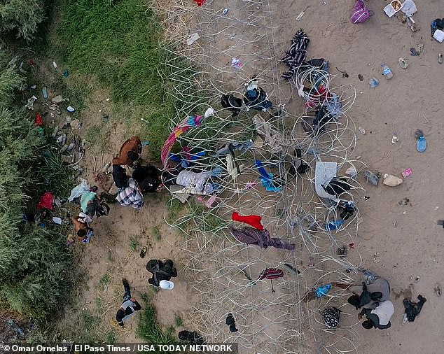 An aerial photo shows desperate migrant families breaking through a wire to enter the US