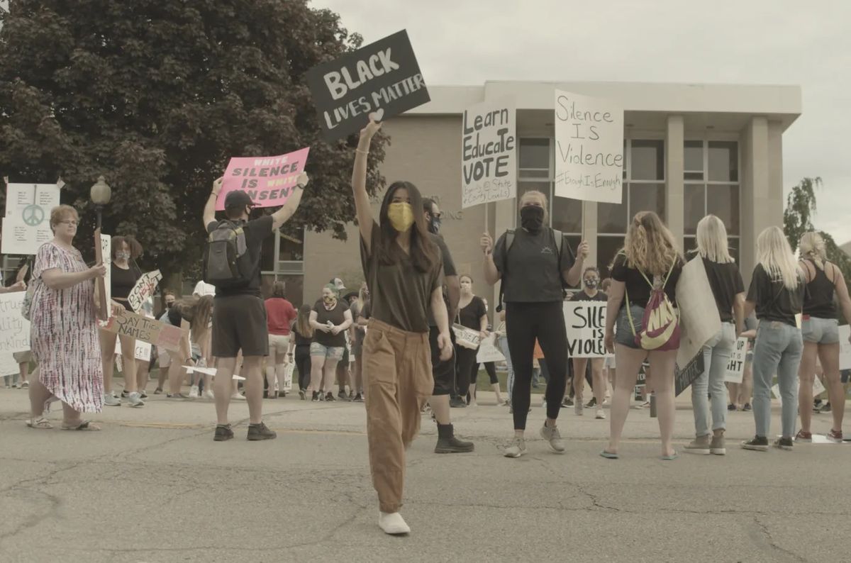 A woman stands among a crowd of protesters holding a sign reading “Black Lives Matter” above her head.