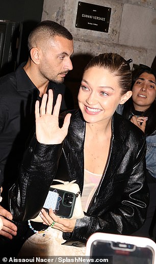 Items: Gigi carried her phone and a small, beige-colored clutch as she waved to excited fans nearby