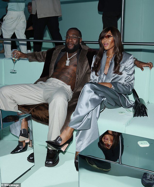 Good form: Naomi accessorized her look with a statement silver necklace as she sat next to Burna Boy, who went shirtless in white pants and a long jacket