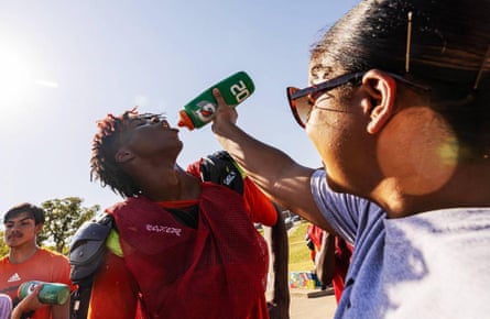 woman pours water from the bottle into the mouth of a football player