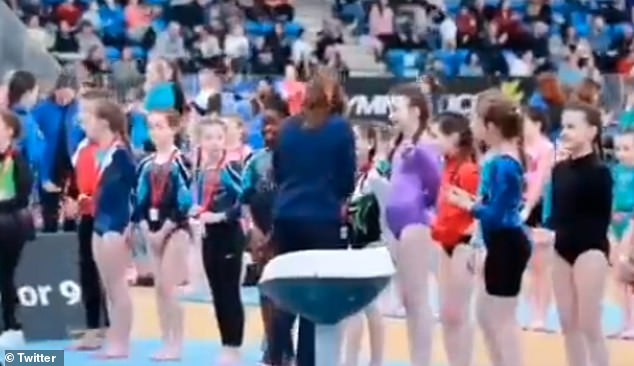 The video shows a line of young gymnasts waiting for their prize, with the little girl excitedly waiting for her medal as her peers receive theirs.