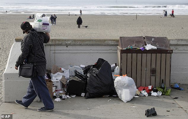 In this Jan. 3, 2019, file photo, a woman walks past trash piled next to a trash can at Ocean Beach in San Francisco