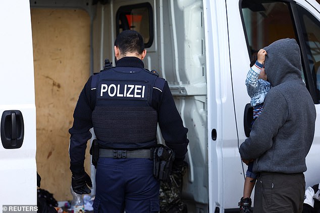 A migrant holds a baby next to a police officer looking inside a van where police found 30 migrants during their patrol along the German-Polish border to prevent illegal migration near Forst, Germany, September 20, 2023