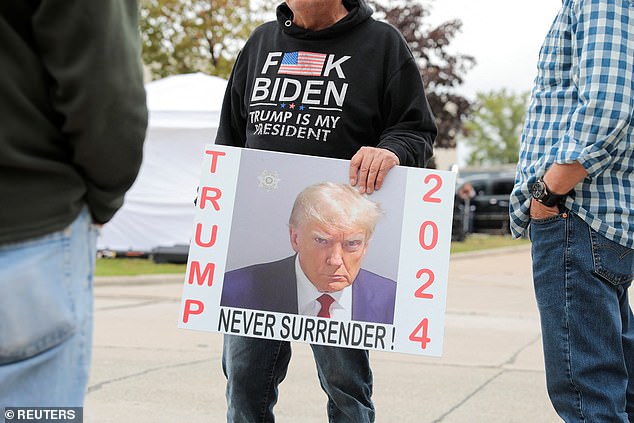 A person holds a sign with Donald Trump's mugshot outside his rally location