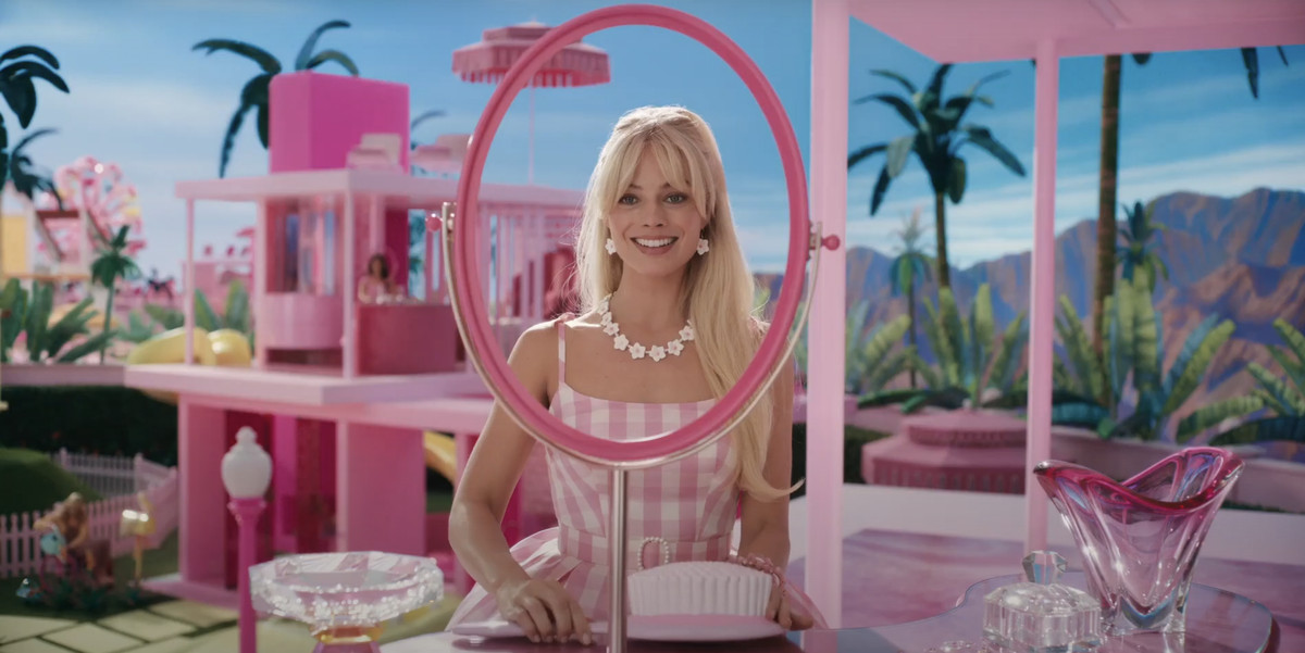 Barbie (Margot Robbie) stares and smiles through a round mirror frame