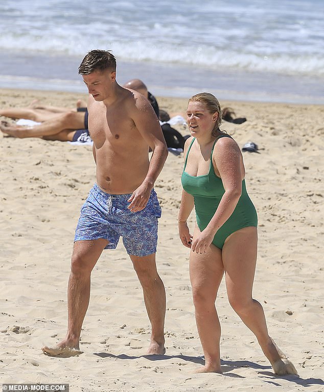 Shane Warne's eldest daughter, 26, flaunted her stunning curves in a bright green swimsuit as she strolled on the sparkling sand with her hunk.  Both in the photo