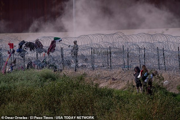 Migrants walk along the north levee of the Rio Grande as they search for an area where they can break the concertina wire constructed by the Texas National Guard outside El Paso