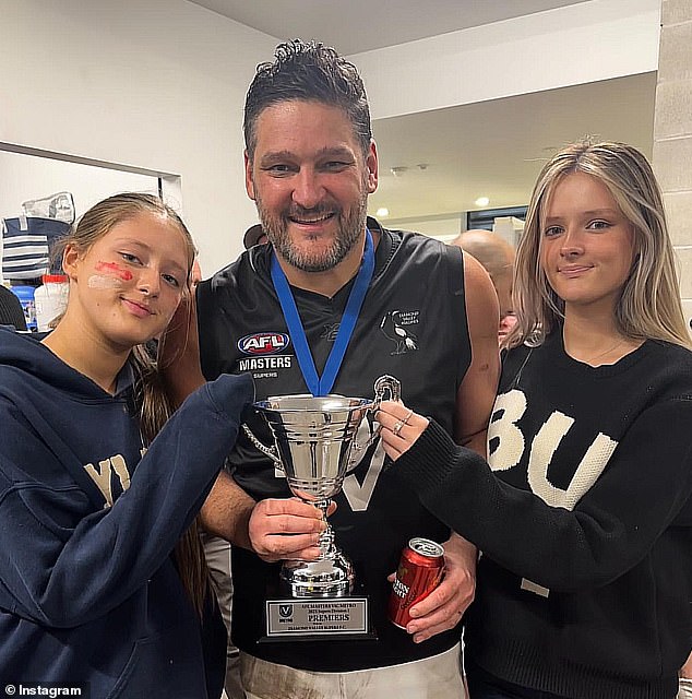 Fevola smiles with the trophy alongside his daughters Leni and Lulu after winning a grand final in his last game of Aussie Rules